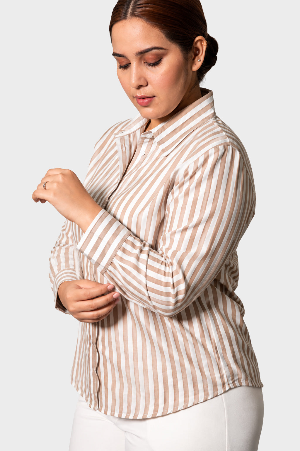 A woman wearing a beige and white vertically striped button-up shirt, shown from the waist up against a light gray studio background.