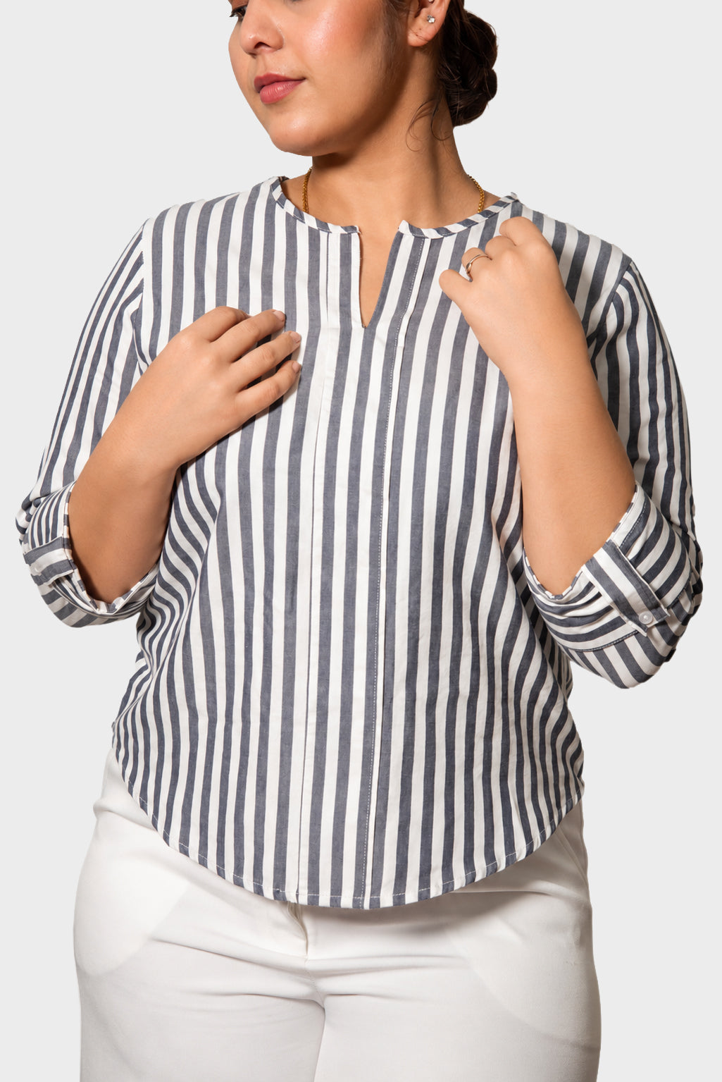 A woman wearing a navy and white vertically striped blouse with a split neckline and white pants, shown from the chest down against a light gray background.
