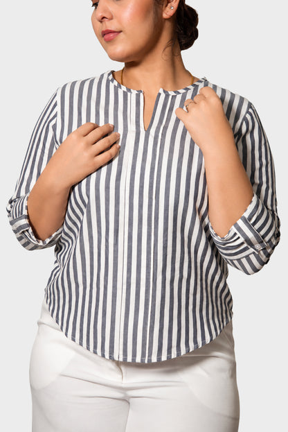 A woman wearing a navy and white vertically striped blouse with a split neckline and white pants, shown from the chest down against a light gray background.