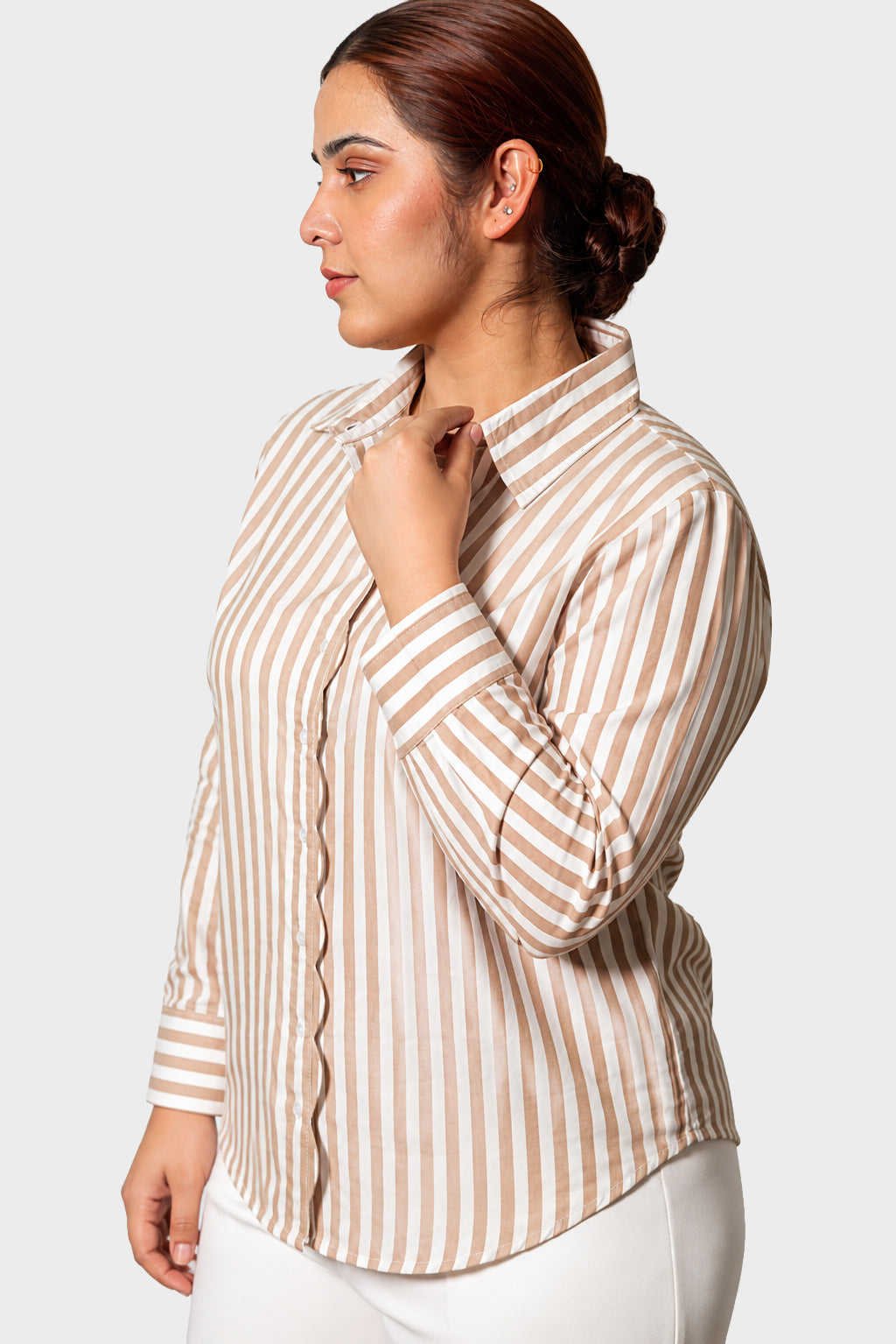 A woman wearing a beige and white vertically striped button-down shirt, shown in a side profile against a light gray studio background.
