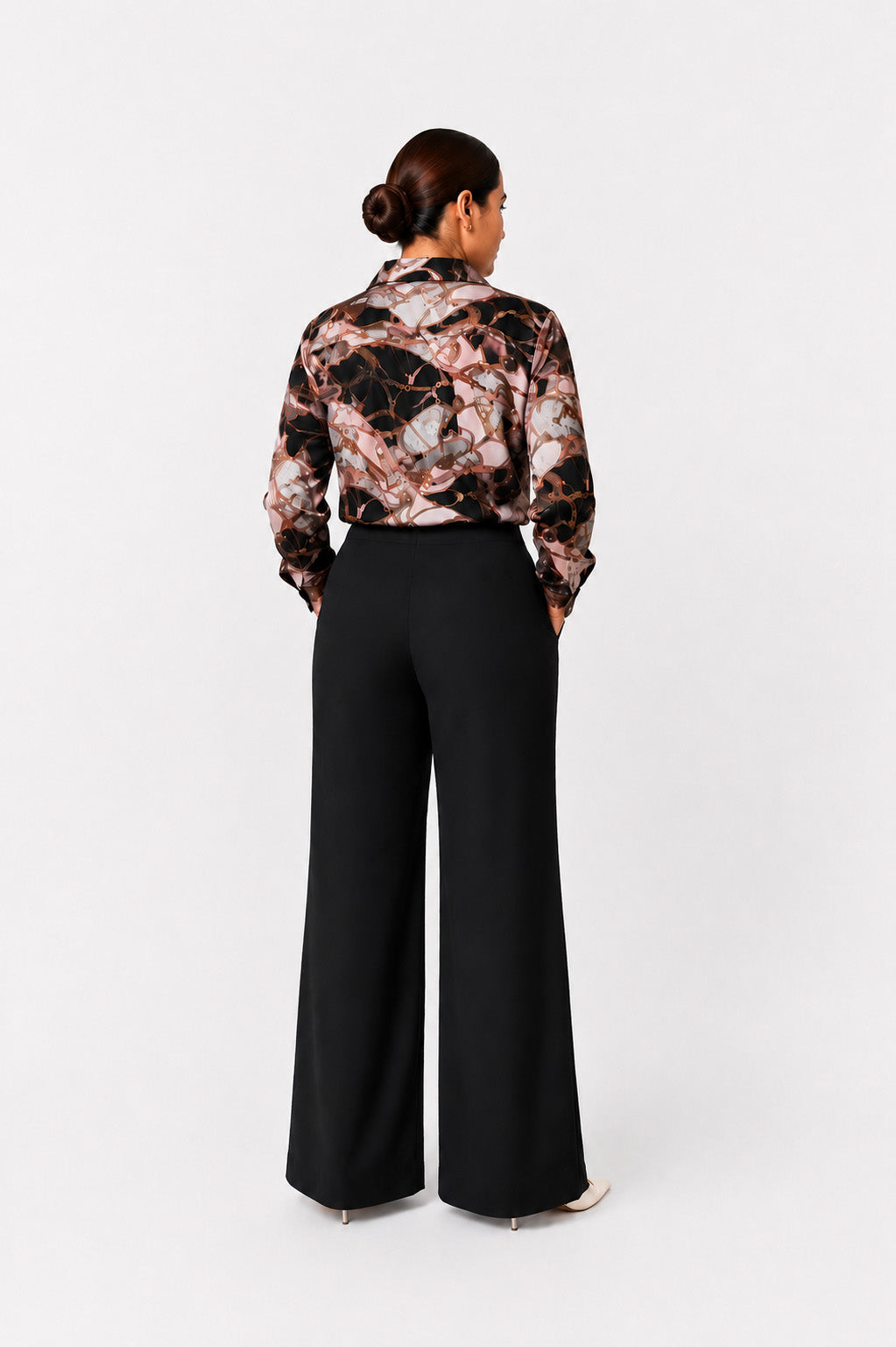 A woman is shown from the back wearing a long-sleeve collared blouse with a black, brown, and beige marble pattern, paired with black wide-leg trousers, against a plain white studio background.