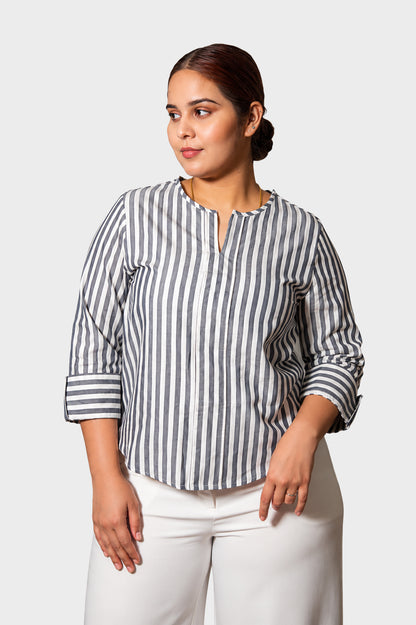 A woman modeling a navy and white vertically striped long-sleeve blouse with a split neckline, paired with white pants, against a light gray studio background.