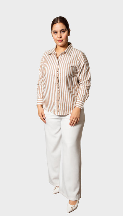 A woman modeling a beige and white vertically striped button-down shirt paired with white wide-leg trousers and white pointed-toe heels, set against a solid light gray background.