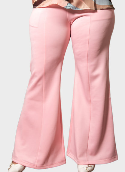 Pink wide-leg pants shown from the back on a model, featuring a smooth fabric and a relaxed flared silhouette, paired with a patterned top and white shoes against a light gray background.