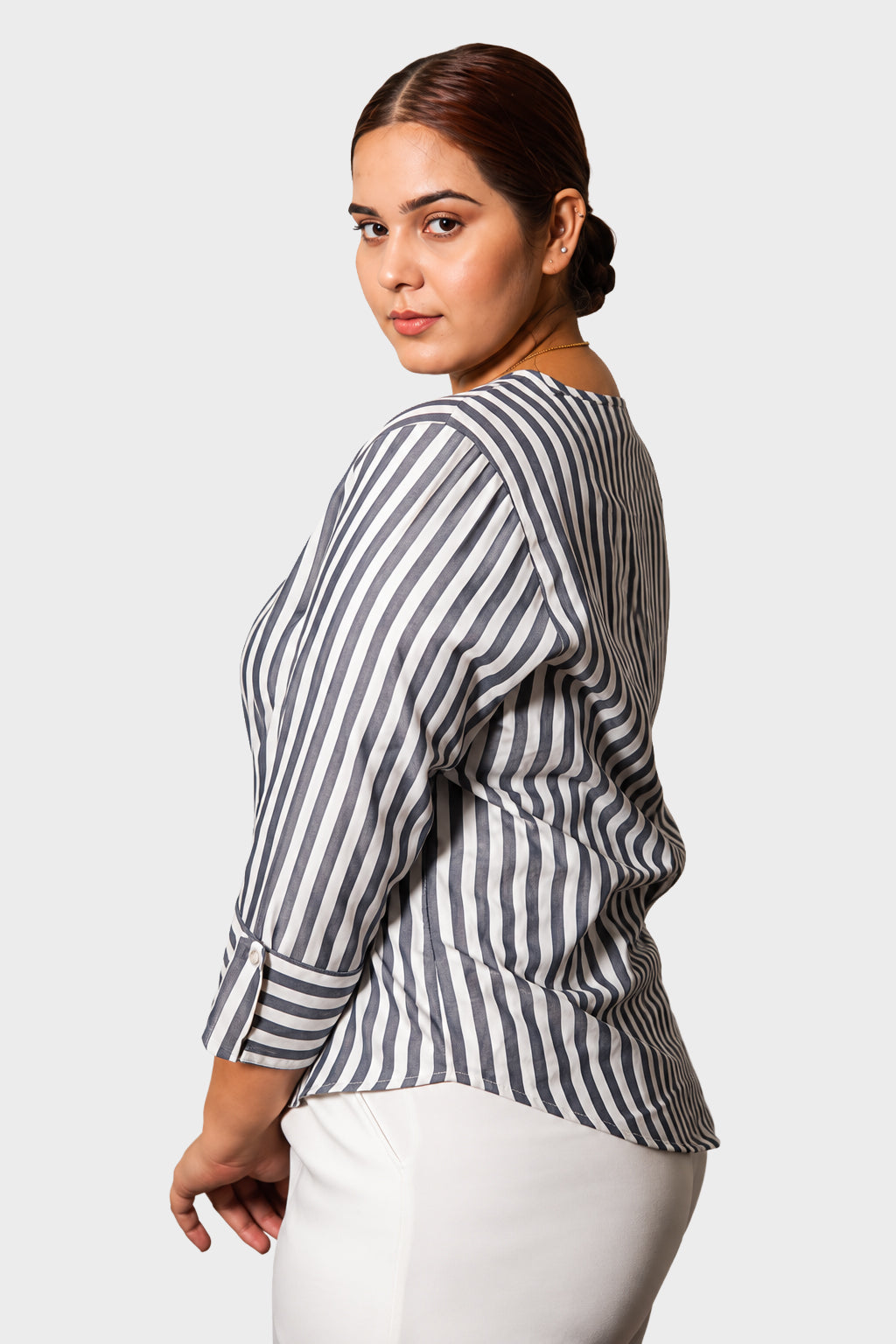 A woman wearing a black and white vertically striped long-sleeve blouse with white pants, photographed against a light gray studio background.