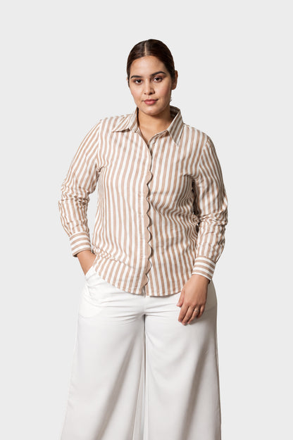 A woman modeling a long-sleeve button-up shirt with vertical beige and white stripes, paired with white wide-leg pants, against a light gray studio background.