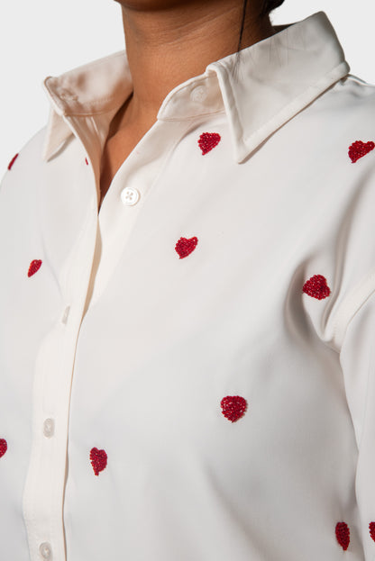 Close-up of a white button-up shirt with small red heart embellishments, worn by a model.