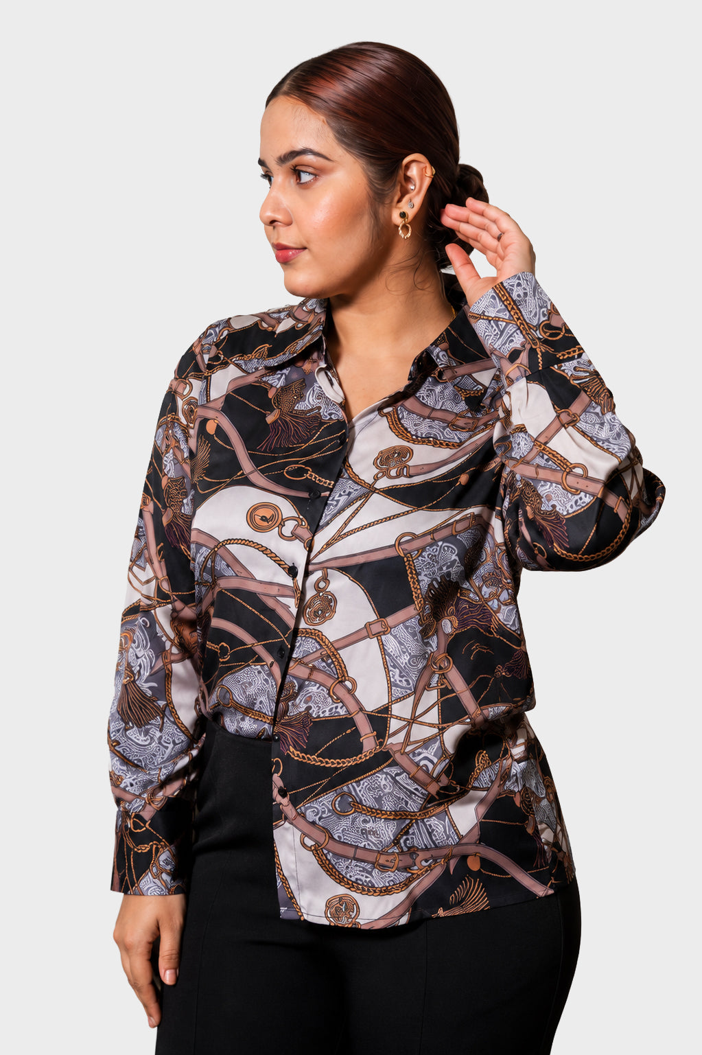 A woman wearing a long-sleeve button-up blouse with an abstract chain-link and rope pattern in black, beige, and brown tones, paired with black pants, set against a plain light gray background.