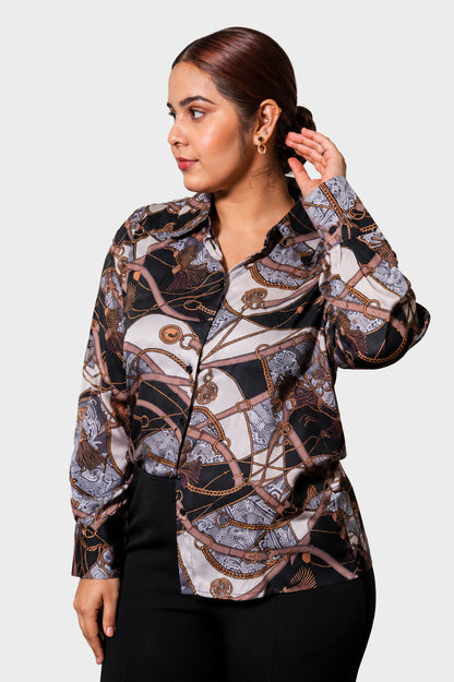 A woman wearing a long-sleeve button-up blouse with an abstract chain-link and rope pattern in black, beige, and brown tones, paired with black pants, set against a plain light gray background.